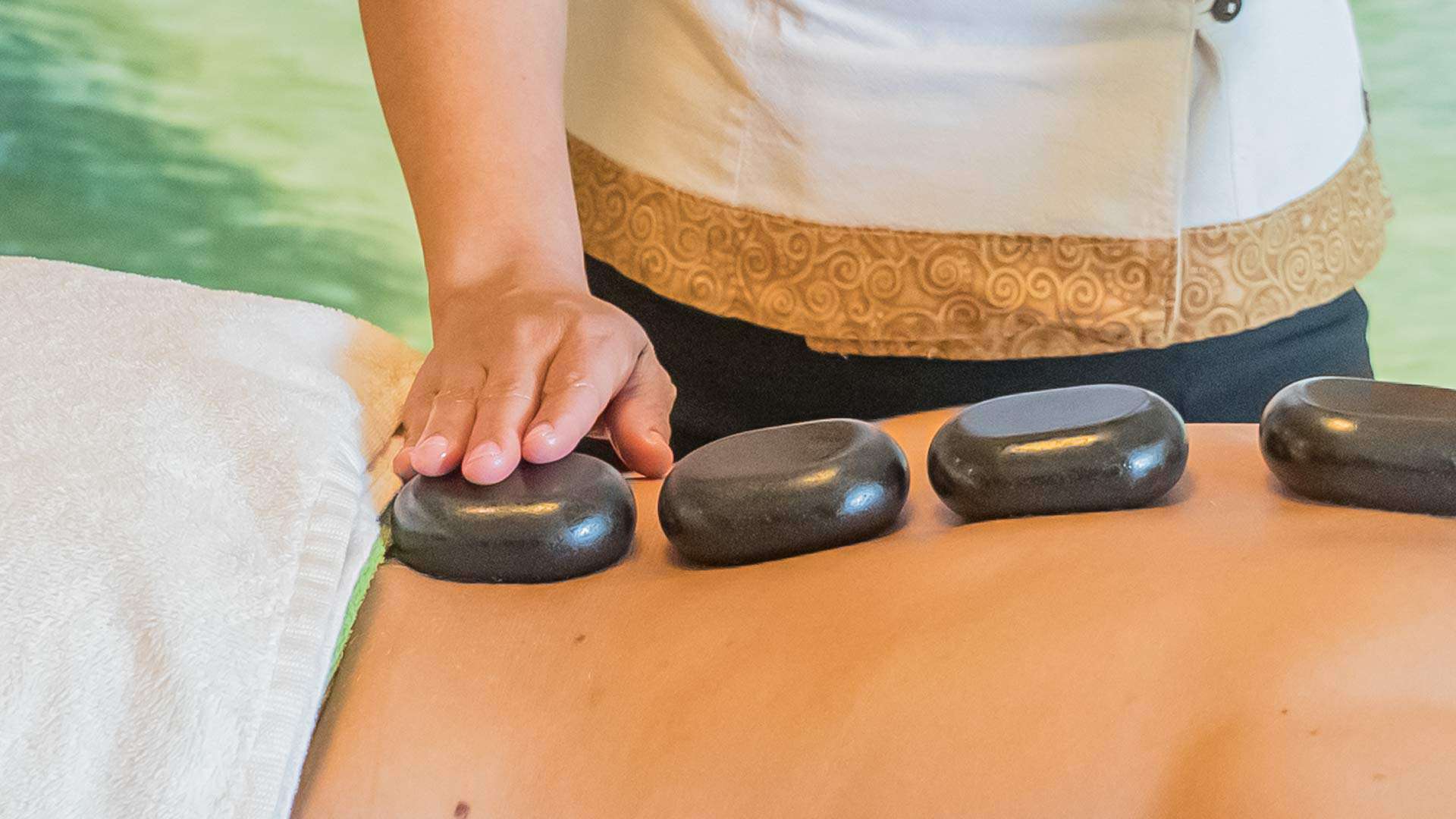 4 Warme Lavasteine liegen auf dem Rücken der Kundin für die Hot Stone Massage.